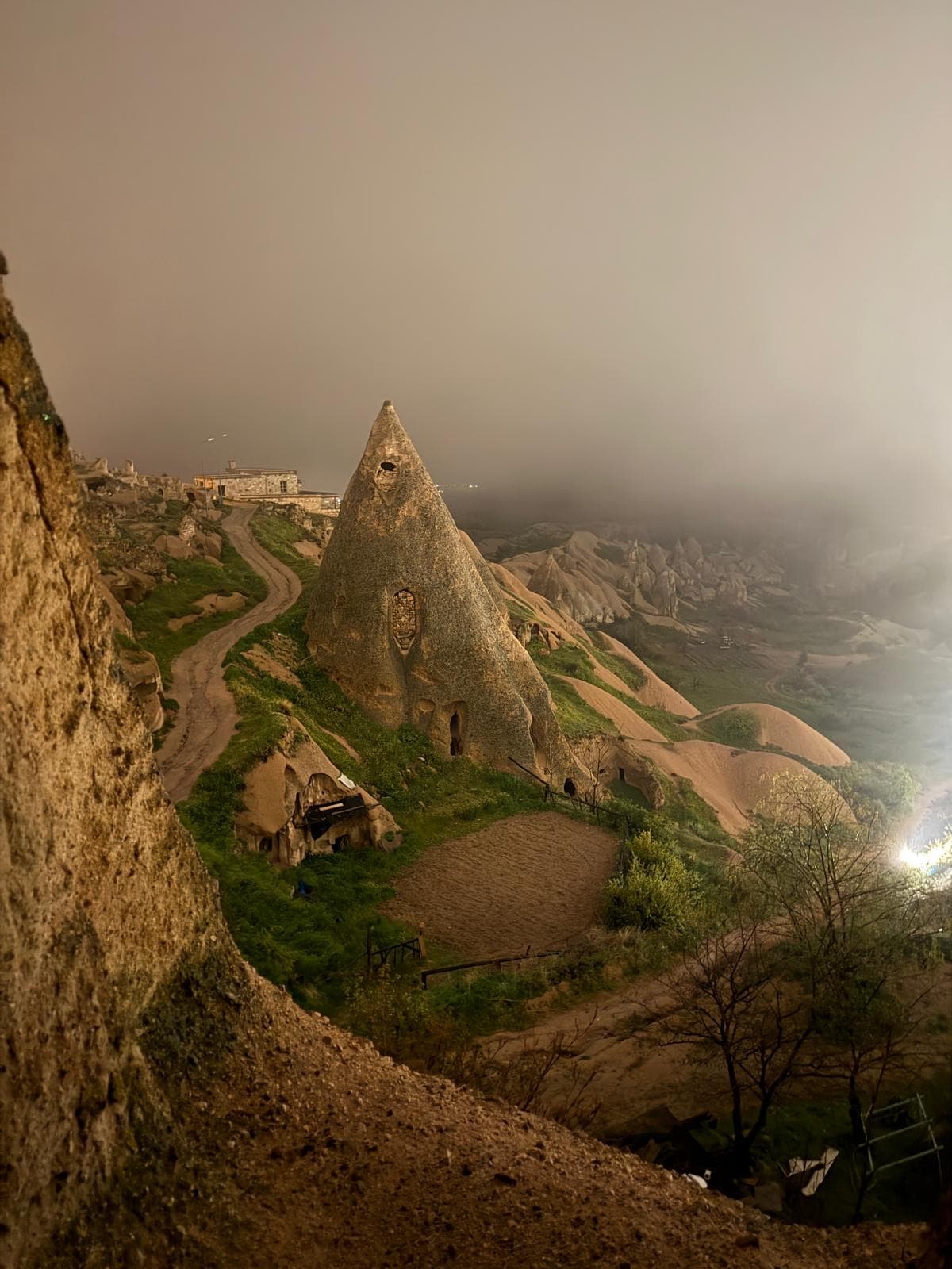 A fairy-chimney formation and terraced gardens under evening mist